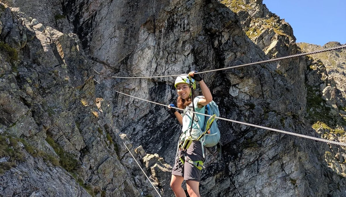 Junge Frau balanciert an Stahlseilen und mit Klettersteig-Set gesichert über kleine Schlucht | © DAV Karlsruhe